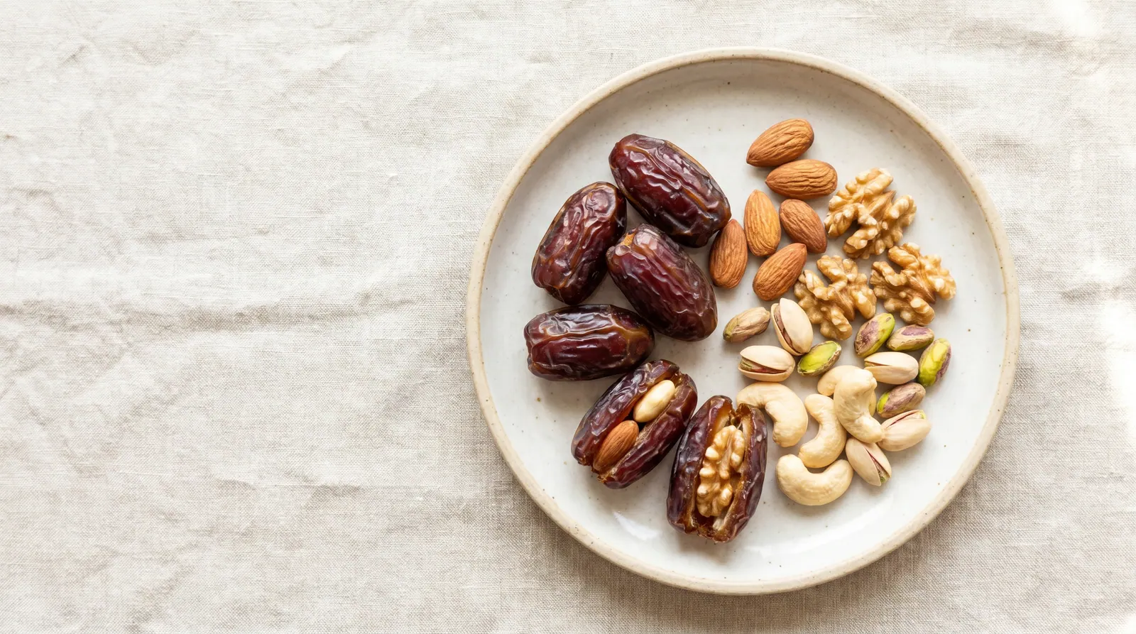 Two dates with a handful of almonds and a cup of yogurt on a wooden surface